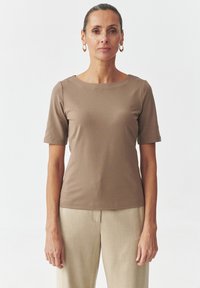 Haut marron à manches courtes avec un col bateau, fabriqué en tissu doux. Porté avec un pantalon beige clair ajusté. Design simple et ajusté sans motifs.