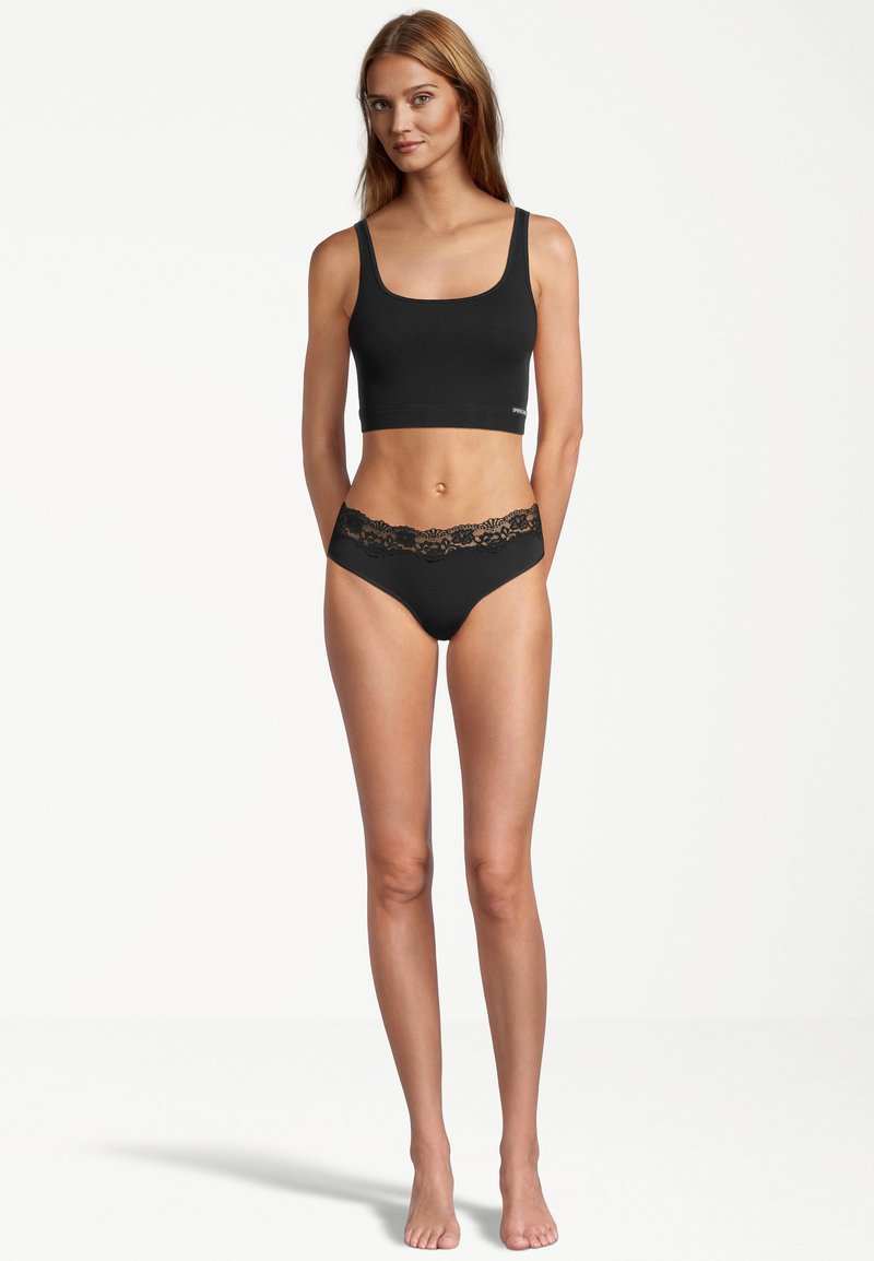 Schwarzes Cropped Top aus glattem Stoff, kombiniert mit schwarzen Unterhosen mit einem Spitzenbund. Beide Teile haben eine enganliegende Passform und ein minimalistisches Design.