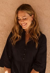 Svart klänning med knappslå och öljettdetaljer på ärmarna, med avslappnad passform och mjuk tygstruktur.