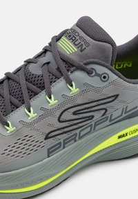Gray athletic shoe with mesh upper and rubber sole, featuring neon green accents, laces, and brand logo on the side and heel.