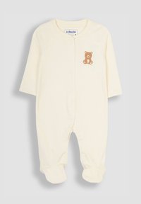 Crèfarbene Babykleidung aus weichem Stoff. Mit langen Ärmeln, Druckknöpfen und einem kleinen braunen Bärenmotiv auf der Brust.
