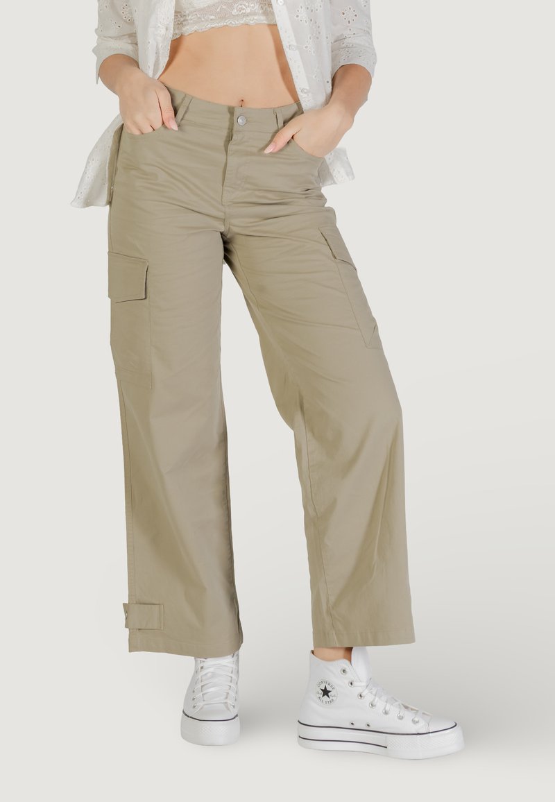 Pantalones cargo caqui con un corte holgado, dos bolsillos frontales y cierre de botón. Combinados con zapatillas blancas para un look casual.