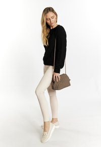 Maglione nero a maglia, pantaloni fitted beige chiaro, scarpe slip-on beige con dettaglio a catena e una borsa a tracolla intrecciata marrone.