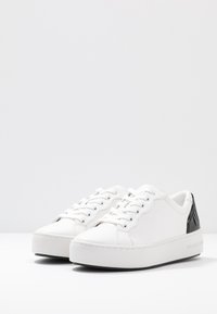 Baskets en cuir blanc à texture lisse, bout arrondi et accents en cuir verni noir au talon. Dotées de lacets plats et d'une semelle épaisse.