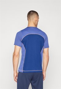Camiseta deportiva de manga corta en azul y púrpura claro con costuras en contraste, que presenta un panel de malla en la espalda para mayor transpirabilidad.