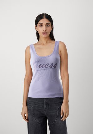 Top tank rib ribattuto lilla con scollo a sorpresa e logo luccicante "Guess" sul davanti, abbinato a jeans scuri a gamba dritta.
