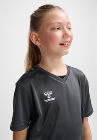Graues Sportshirt mit kurzen Ärmeln und V-Ausschnitt. Verfügt über ein weißes "hummel"-Logo und ein glattes, leichtes Material.