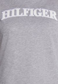 Camiseta gris hecha de algodón suave con cuello redondo, que presenta texto bordado en blanco que dice "HILFIGER" en el pecho.