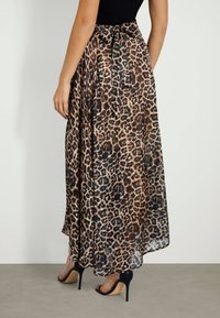 Gonna maxi in tessuto trasparente con stampa leopardata, caratterizzata da un dettaglio in vita annodato e un design fluente, abbinata a scarpe con tacco alto nere.