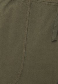 Shorts in tessuto verde oliva con una texture morbida, caratterizzati da una cucitura visibile e un dettaglio con cordino. Il tessuto sembra leggero e traspirante.