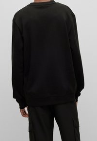 Czarna bluza z okrągłym dekoltem, wykonana z miękkiego materiału. Charakteryzuje się ściągaczami na mankietach i dole oraz luźnym krojem. Widok z tyłu ukazuje bezszwowy design ramion.