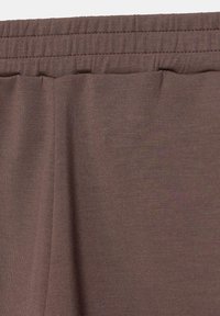 Gros plan sur une ceinture élastique marron sur un tissu doux et léger avec des coutures et une texture visibles.
