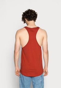 Top sin mangas color burdeos con diseño de espalda nadadora, hecho de una tela suave. Presenta un dobladillo redondeado y un corte relajado, que resalta la espalda y los hombros.