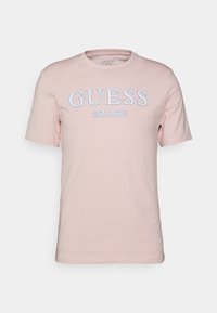 Růžová bavlněná tričko s krátkým rukávem, na přední straně s bílým logem "GUESS" a textem "EST. 1981". Kolo krk design.