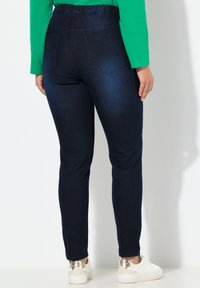 Ciemnoniebieskie, elastyczne jeansy z wysokim stanem i tylnymi kieszeniami. Nogawki są dopasowane, zestawione z białymi trampkami z metalicznym akcentem.