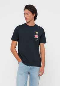 Marineblauwe katoenen T-shirt met een ronde halslijn en korte mouwen, voorzien van een kleurrijke geborduurde rozen- en kroonembleem op de borst.