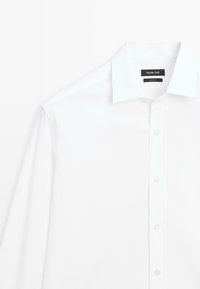 Camicia bianca a maniche lunghe con colletto classico, chiusura frontale con bottoni e tessuto liscio e croccante.