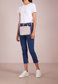 Borsa a mano rettangolare rosa chiaro con logo "HUGO" in rilievo, manico corto e tracolla regolabile, abbinata a jeans blu e sneakers bianche.