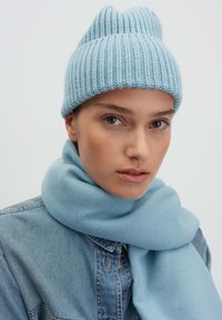 Lichtblauwe gebreide beanie met textuur ribbeling, voorzien van een onderscheidende kroon met twee punten. Vergezeld van een zachte, bijpassende lichtblauwe sjaal.
