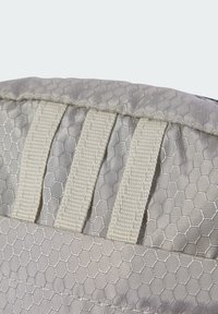 Tessuto grigio a motivo esagonale con due cinghie bianche e un bordo testurizzato. Vista ravvicinata che evidenzia il design e il materiale.