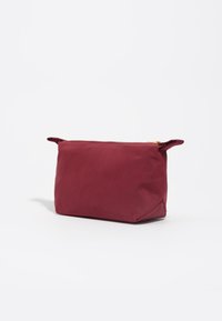 Bolsa de cosméticos color burdeos con forma rectangular, hecha de tejido suave, con un cierre dorado y dos asas cortas a los lados.