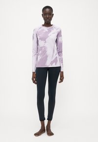 Dlouhý rukáv purpurové tričko s tie-dye vzorem, kombinované s černými legínami s texturovaným panelem na dolní části nohavic.