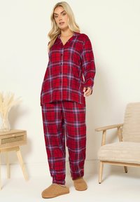 Röd rutiga pyjamasset med knapp-up topp och löst sittande byxor. Mjuk tyg med lila och svarta accenter, i kombination med beige fluffiga tofflor.