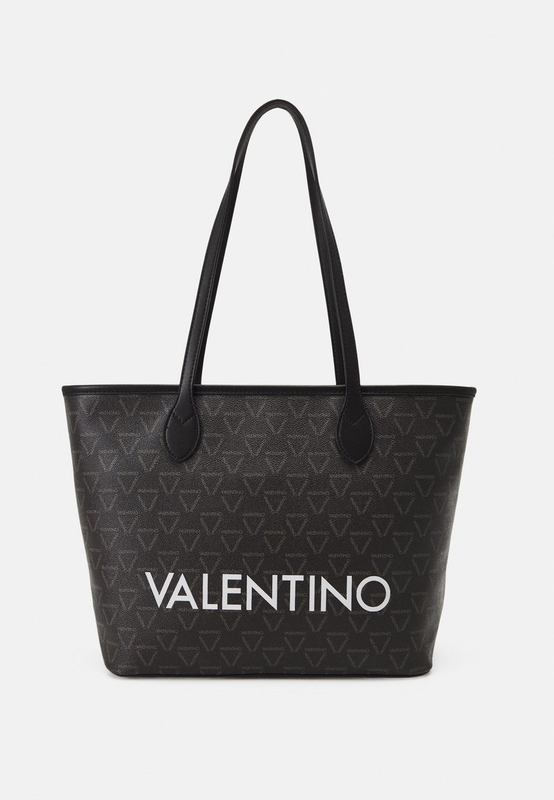 Black Valentino tote bag with repeating logo pattern and large white "VALENTINO" text, featuring two long shoulder straps.