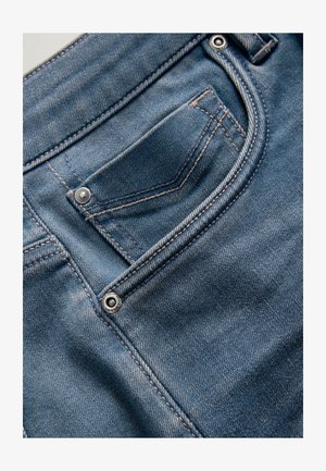 Niebieskie dżinsy wykonane z denimu, z przednią kieszenią zapinaną na srebrny guzik. Tkanina ma wyblakłą fakturę z kontrastującymi przeszyciami.