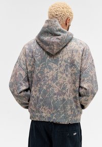 Hætte sweatshirt i dæmpet camouflage mønster med nuancer af grøn, beige og grå. Løs pasform med ribbet kant ved håndled og kant.