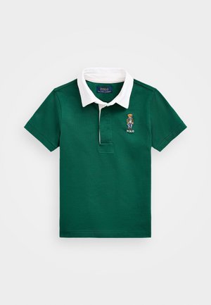 Polo vert à manches courtes avec col blanc, broderie d'un ours portant une veste et un jean sur la poitrine gauche, et étiquette Polo Ralph Lauren à l'intérieur du col.