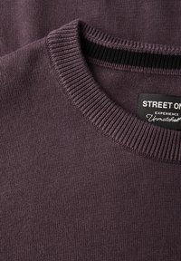 Lila gestrickter Pullover mit einem gerippten Rundhalsausschnitt und glatter Textur. Enthält ein Etikett mit der Marke "STREET ON".