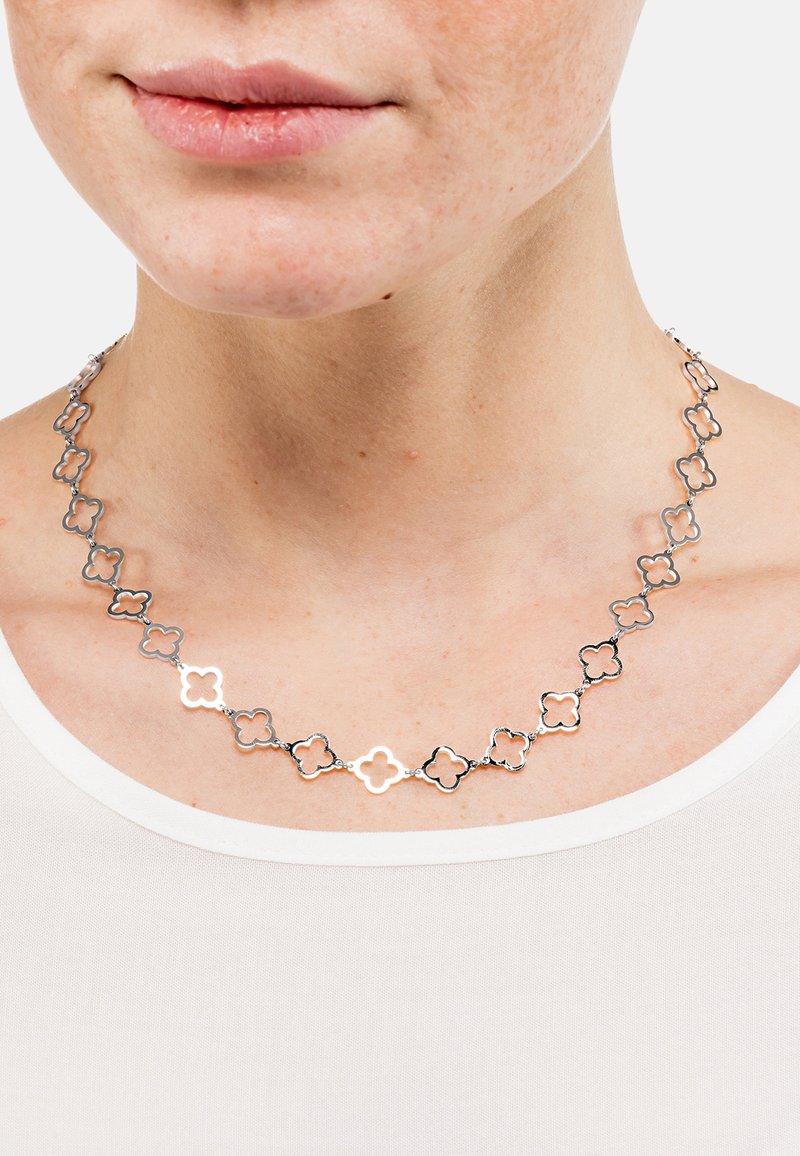 Collar de metal plateado con formas florales interconectadas, alternando entre diseños huecos y sólidos, descansando sobre un cuello descubierto.