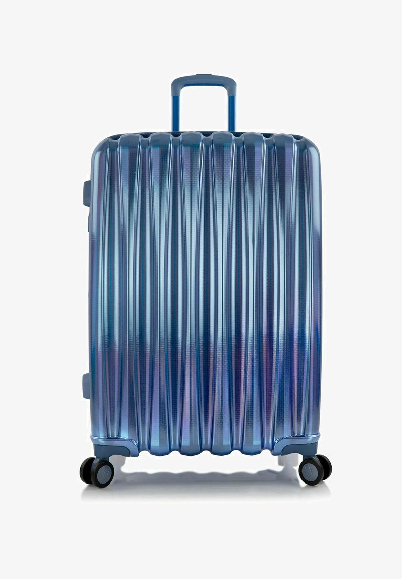 Valise rigide en dégradé de bleu avec des rainures verticales, une poignée télescopique et quatre roues noires pour la mobilité.