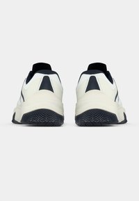 Fehér és tengerészkék atlétikai cipők texturált talppal, elegáns kialakítással, párnázott szegéllyel, valamint minimális díszítéssel az oldalukon és hátulján.