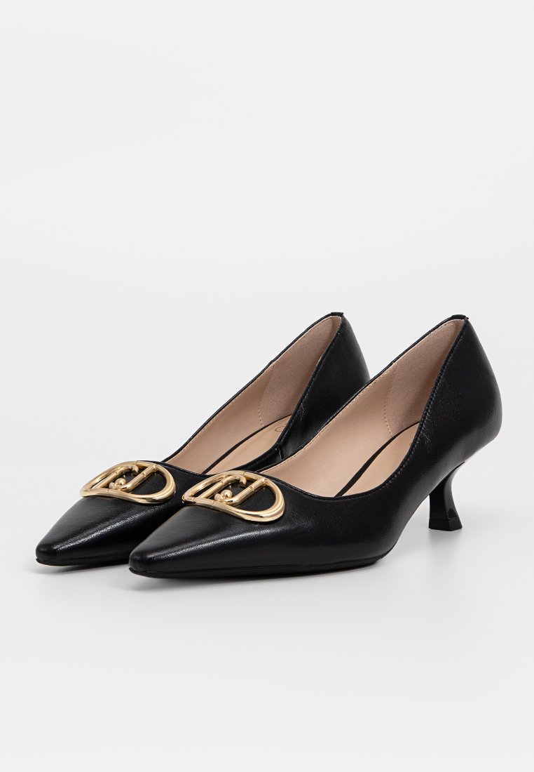 Tacones kitten de punta negra de cuero con interior beige y hebilla decorativa dorada en la punta, mostrados sobre un fondo blanco.