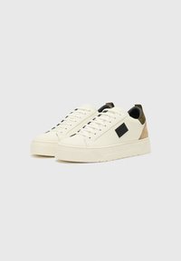Weiße Sneakers aus strukturiertem Leder, mit einem schwarzen Logo-Patch, einem kontrastierenden olivgrünen Fersenloop und einer dicken Gummisohle.