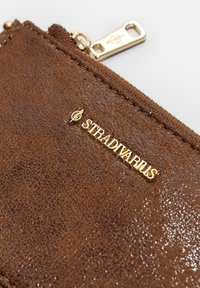 Braunes Strukturportemonnaie mit einem goldenen Reißverschluss und Hardware. Verfügt über ein goldenes "Stradivarius"-Logo auf der Vorderseite. Kompakte Form und schlankes Design.