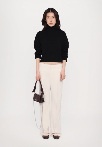 Black ribbed turtleneck sweater, cream wide-leg trousers, dark flat shoes, and a small burgundy handbag with chain detail.