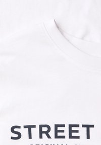 Biała bawełniana koszulka z okrągłym dekoltem i czarnym nadrukiem z napisem „STREET ORIGINAL”. Gładka faktura.