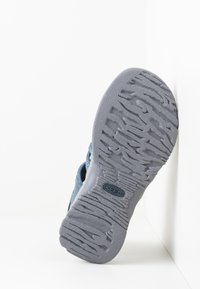 Blue shoe with a flexible gray rubber outsole featuring textured tread patterns. The upper is made of breathable fabric, designed for comfort.