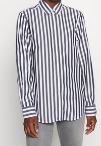 Skjorta med lång ärm, knäppning framtill och vertikala marinblå och vita ränder, i en blandning av bomull, med krage och enkel knapp på ärmsluten.