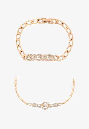 Dwie złote bransoletki łańcuchowe z przezroczystymi kamieniami ozdobnymi, jedna z wzorem spiralnym, druga z okrągłą klamrą jako centralnym elementem.