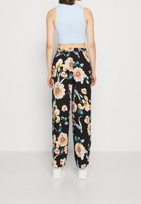 Pantalons à jambes larges imprimés floraux en noir, avec de grandes fleurs orange et jaunes, dotés d'une taille élastique et d'une texture douce.