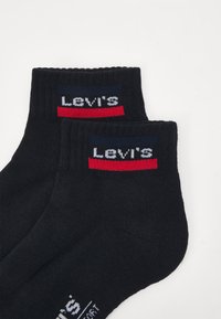 Schwarze Baumwollsocken mit einem gerippten Bündchen, auf dem das "Levi's"-Logo in Weiß sowie rote und marineblaue Streifen akzentuiert sind. Glatte Textur, Knöchellänge.