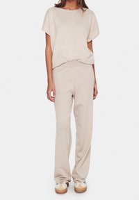 Beige loungewear-set bestående av en lös topp med korta ärmar och matchande vida byxor i mjukt stickat material. Avslappnad design med ribbade ärmslut.