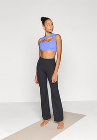 Μπλε cropped τοπ με λεπτομέρεια κοψίματος, συνδυασμένο με μαύρο καμπανέ κολάν. Λείο ύφασμα, εφαρμοστό, με ψηλή μέση, κατάλληλο για αθλητική ένδυση.
