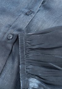 Donkerblauwe blouse met een gladde, glanzende textuur, knoopsluiting en geplooide details aan de zijkant.