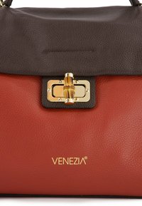 Leather handbag featuring a brown top flap, red bottom, gold hardware with a bamboo accent, and "VENEZIA" logo embossed in gold.