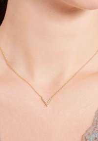 Gouden ketting met een V-vormige hanger die is ingelegd met kleine heldere stenen, rustend op een gladde halslijn met een zachte huidtextuur.